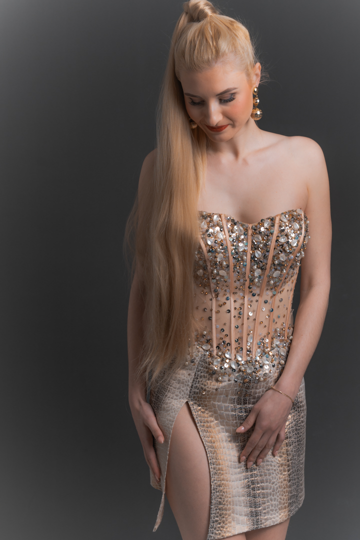 Foto in posa della donna con abito elegante, seduta su una sedia nera, con tacchi alti e uno sguardo sofisticato
