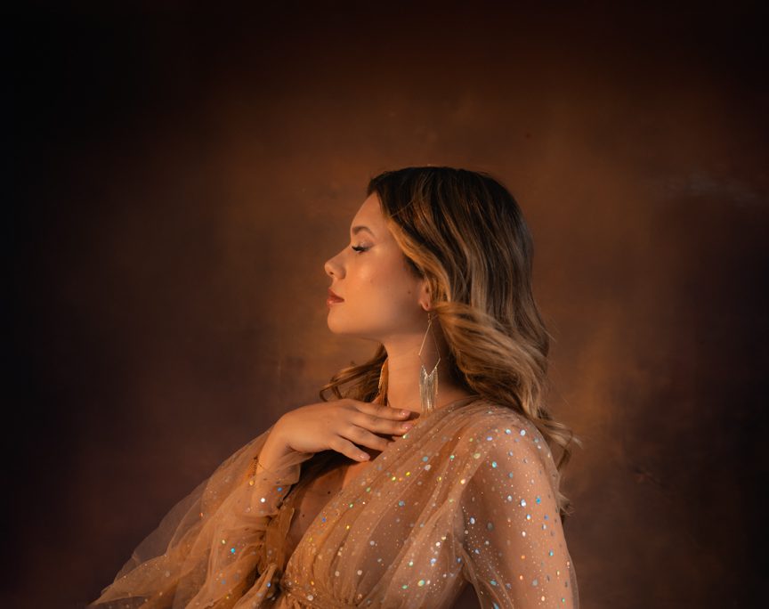 Donna incinta con un elegante abito in tulle color champagne con dettagli scintillanti, posa in diverse angolazioni in uno studio fotografico con sfondo scuro e piante.